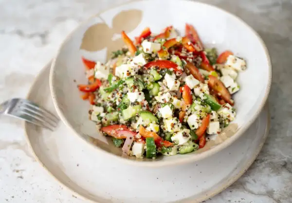Salade quinoa colorée avec des dés de feta, concombre, poivrons rouges et herbes fraîches. Un plat sain et savoureux.