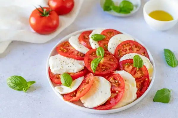 Salade Caprese al limone : rondelles de tomates fraîches, mozzarella crémeuse et feuilles de basilic, assaisonnée d'un filet d'huile d'olive.