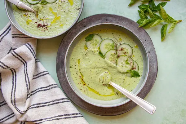 Deux bols de soupe froide crémeuse aux concombres, garnie de rondelles de concombre, de menthe et d'un filet d'huile d'olive.