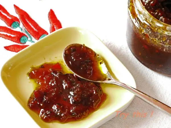 Une cuillère sert une délicieuse confiture de piment, avec un bocal et des piments rouges brodés en arrière-plan.