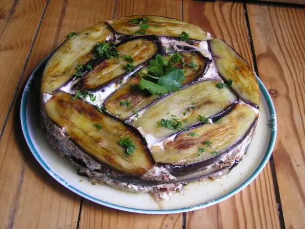 Moussaka ronde, une délicieuse moussaka ricetta, garnie d'aubergines grillées et de persil frais, sur une assiette blanche à bordure verte.