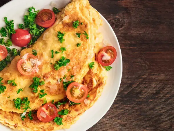 Une savoureuse omelette grecque, garnie de tomates cerises et de persil frais, sur une assiette blanche.