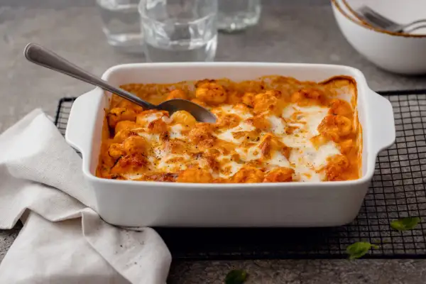Un plat blanc rempli de gnocchi alla sorrentina, gratinés au fromage fondant et à la sauce tomate. Une cuillère est prête à servir.
