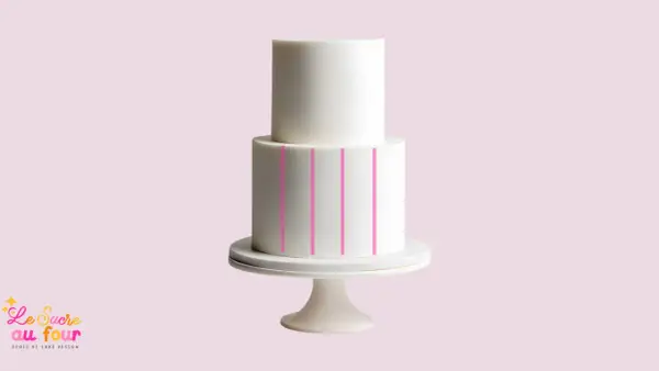 Un gâteau blanc à deux étages sur un présentoir, avec des lignes roses indiquant comment faire un gâteau de couche.