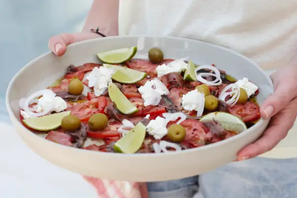 Salade colorée avec tomates, olives, anchois, oignons rouges, quartiers de citron vert et éclats de ricotta. Une idée recette ricotta fraîche et estivale.