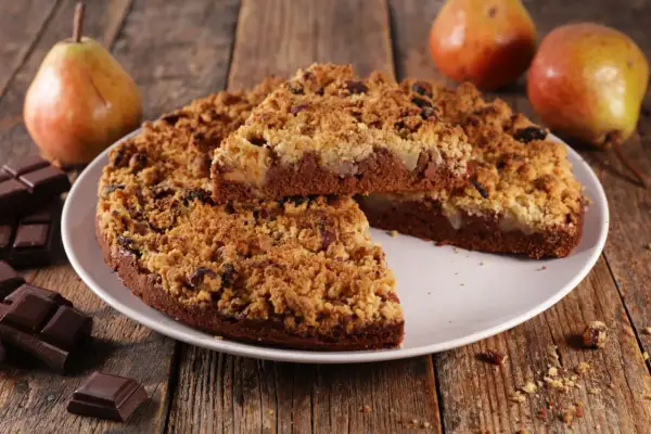 Une délicieuse tarte aux poires, avec une croûte croustillante et des morceaux de chocolat noir, est présentée sur une assiette blanche.