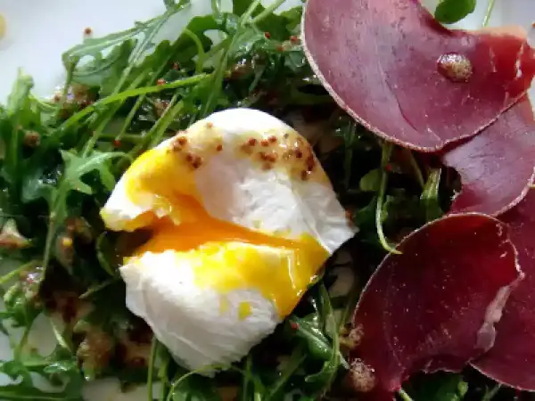Salade lyonnaise avec œuf poché coulant, roquette et fines tranches de viande séchée.