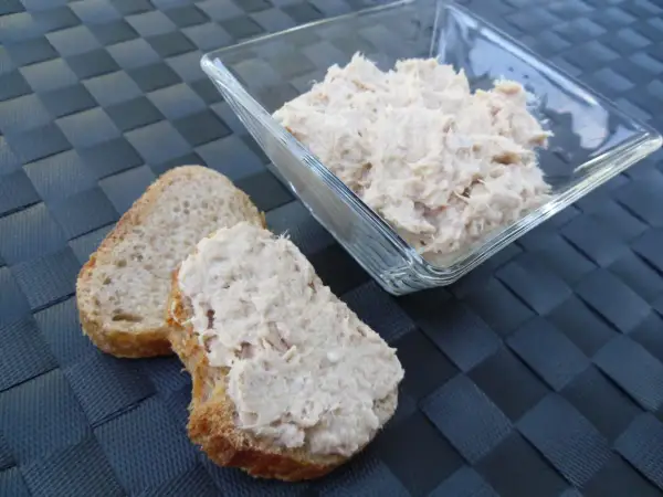 Deux tranches de pain de campagne garnies de rillettes de thon, avec un bol de rillettes de thon en arrière-plan.