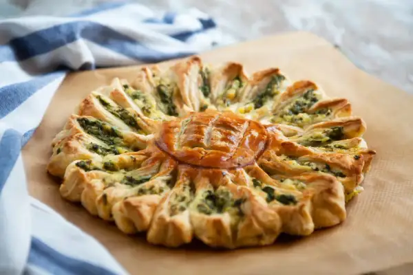 Un feuilleté apéro en forme de soleil, garni d'épinards et de fromage, prêt à être dégusté.