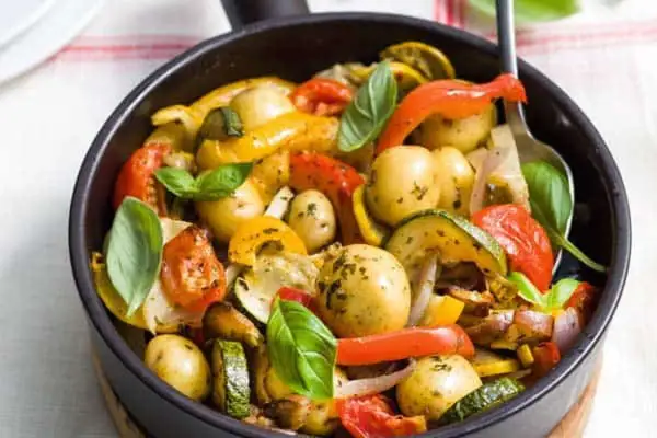 Poêlée de légumes colorés avec des pommes de terre grenaille, poivrons, courgettes et tomates, garnie de basilic frais.
