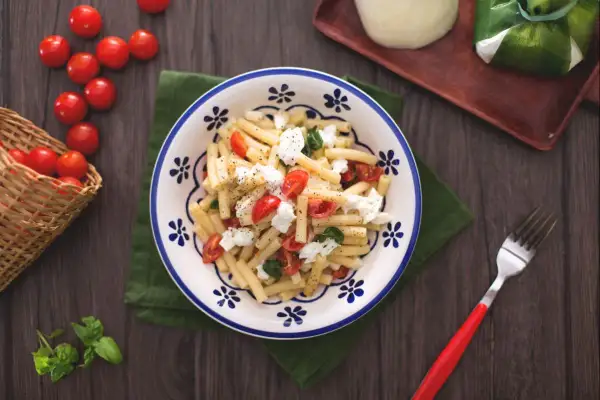 Un plat de pâtes alla checca, garni de tomates cerises fraîches, de mozzarella et de basilic, prêt à être dégusté.