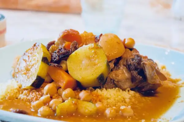 Un plat généreux de couscous algérien, garni de légumes tendres, de pois chiches et de viande savoureuse, baignant dans une sauce parfumée.