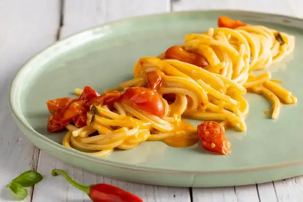 Un plat de scarpariello pasta, des spaghettis aux tomates cerises et au piment rouge, sur une assiette verte.