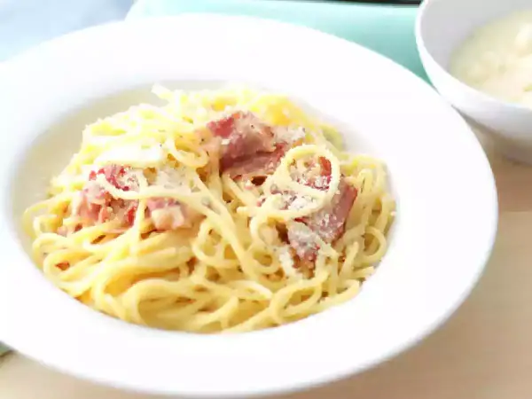 Un plat de pâtes à la carbonara crémeuses, garni de lardons croustillants et de parmesan râpé, prêt à être dégusté.