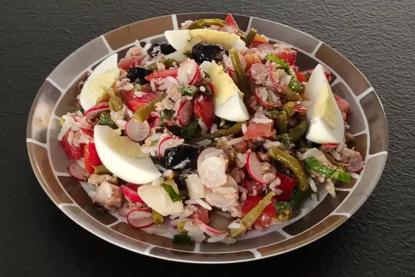 Salade niçoise revisitée avec du riz, garnie d'œufs durs, de thon, de haricots verts, de tomates, de radis et d'olives noires.