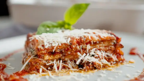 Tranche d'aubergine parmigiana, garnie de parmesan râpé et d'une feuille de basilic frais. Un délice italien.
