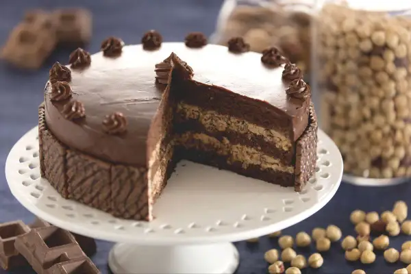Gâteau gaufrette chocolat noisette, une tranche coupée révèle ses couches gourmandes. Des noisettes et des carrés de chocolat complètent ce délice.