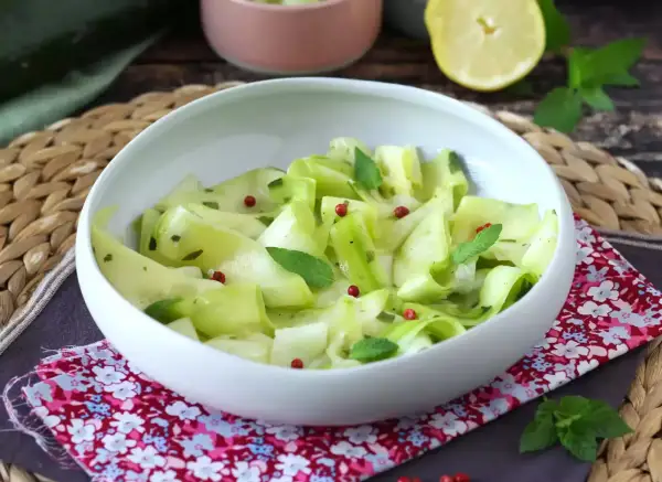 Salade fraîche de courgettes crues marinées au vinaigre, parsemée de baies roses et de menthe.