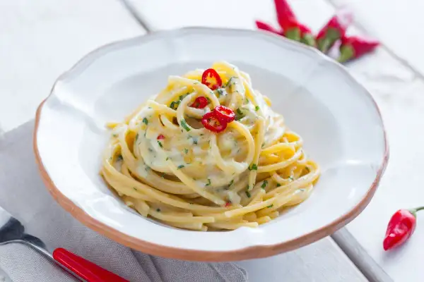 Un plat de spaghetti carrettiera crémeux, garni de piments rouges frais et de persil, prêt à être dégusté.