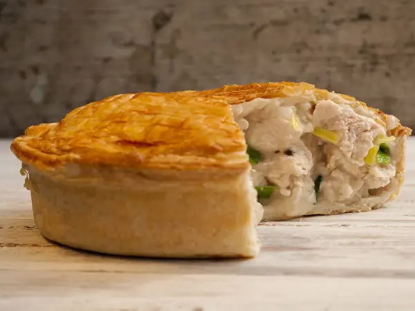 Une tourte au poulet dorée et croustillante, coupée pour révéler une garniture crémeuse et généreuse de poulet et de légumes verts.