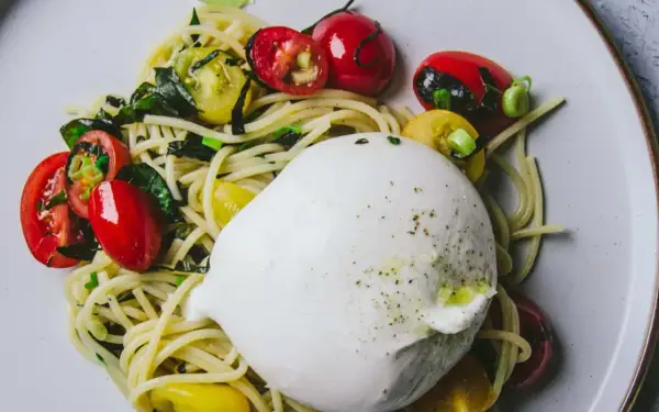 Délicieuse recette avec burrata : pâtes, tomates cerises rouges et jaunes, et herbes fraîches sur une assiette.