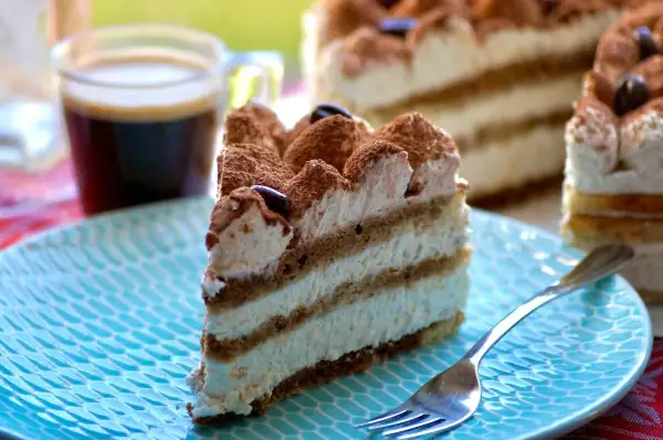 Une part de tiramisu gâteau, crémeux et aérien, saupoudrée de cacao, avec un café noir en arrière-plan.