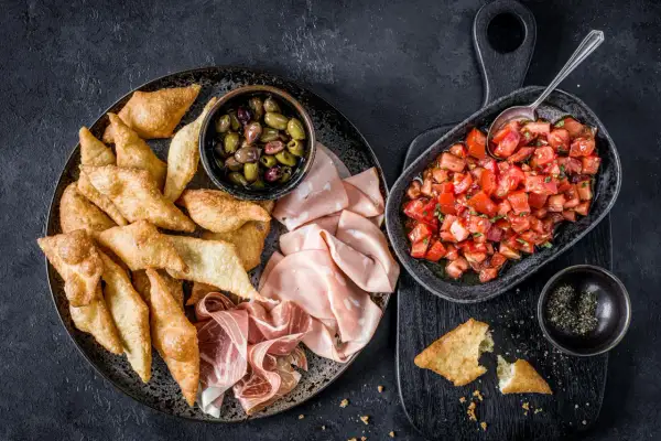 Assiette de gnocco fritto croustillant, olives, mortadelle et prosciutto, avec une salade de tomates fraîches.