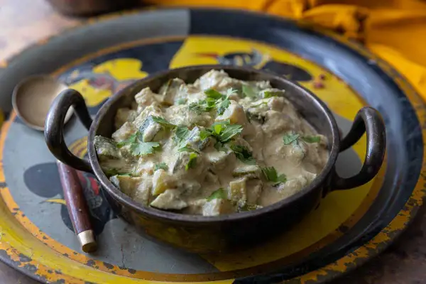 Un plat de courgettes au curry crémeux, garni de coriandre fraîche, servi dans un bol en métal sur un plateau décoré.