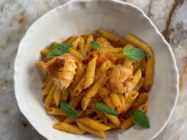 Un plat de pâtes aux langoustines, garni de feuilles de basilic frais et d'une sauce onctueuse. Un délice pour les amateurs de fruits de mer.