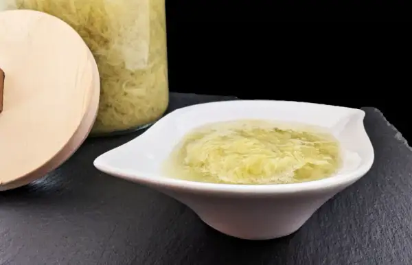 Une coupelle blanche présente une compote de rhubarbe onctueuse, avec un bocal en verre rempli de cette même compote en arrière-plan.