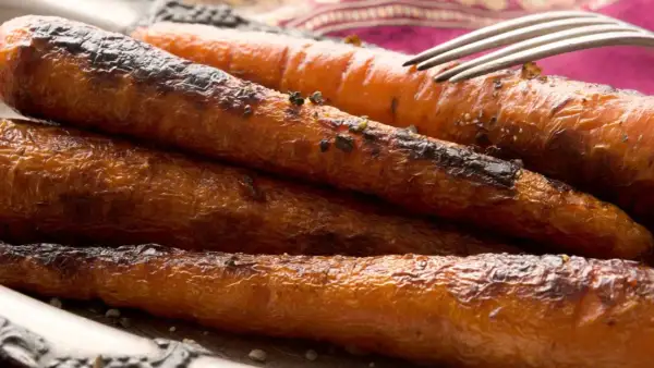 Carottes rôties, caramélisées et légèrement grillées, servies sur une assiette avec une fourchette. Un délice croustillant et savoureux.