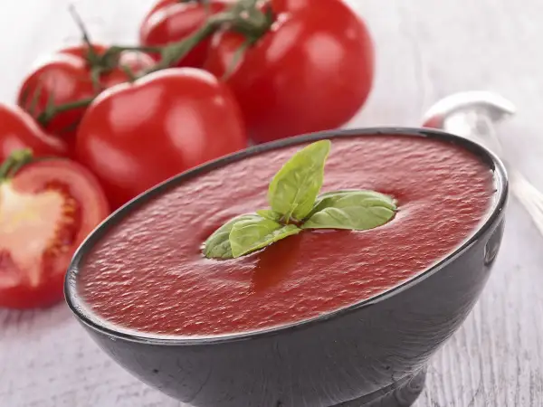 Un bol de soupe de tomates fraîches, garni de basilic, avec des tomates mûres en arrière-plan.