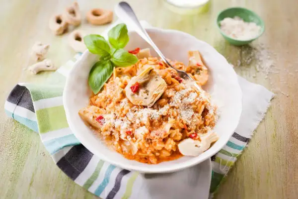 Un délicieux risotto pesto rosso, garni d'artichauts et de basilic frais, saupoudré de parmesan.
