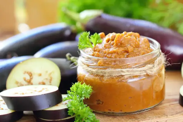 Un pot de caviar d'aubergine, prêt à être dégusté, avec des aubergines fraîches et des herbes. Une recette italienne simple et savoureuse.