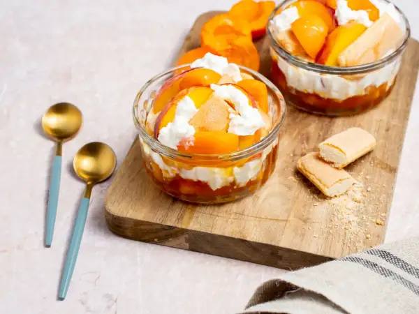 Deux coupes de dessert healthy aux pêches et crème fouettée, garnies de biscuits à la cuillère.