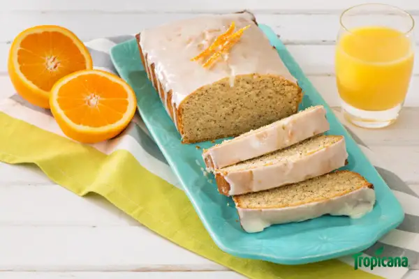 Un délicieux pain d'orange glacé, garni de zestes d'orange, servi avec des moitiés d'orange et un verre de jus d'orange.