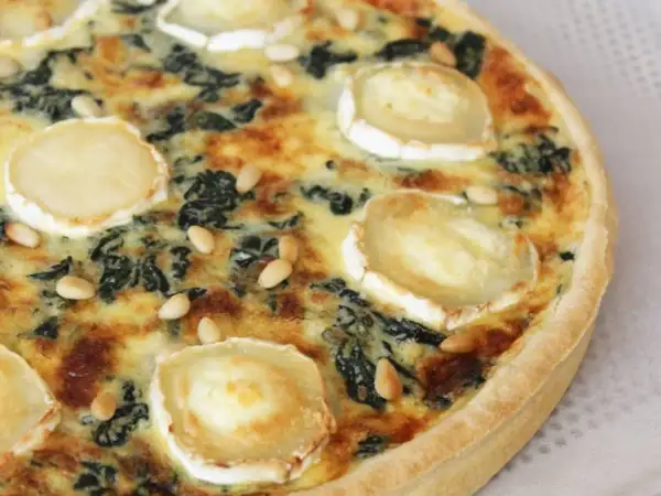 Quiche épinard chèvre, garnie de rondelles de fromage de chèvre et de pignons de pin, prête à être dégustée.