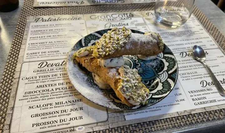 Deux cannoli siciliens garnis de crème et de pistaches concassées, saupoudrés de sucre glace.
